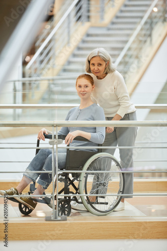 Portrait of senior nurse standing near the young disabled woman in wheelchair and they looking at camera at hospital