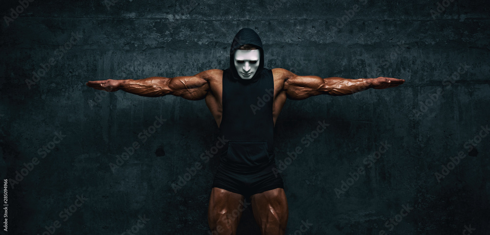 Mysterious Muscular man hiding behind mask Flexing Muscles. Bodybuilder with mask on his face posing.