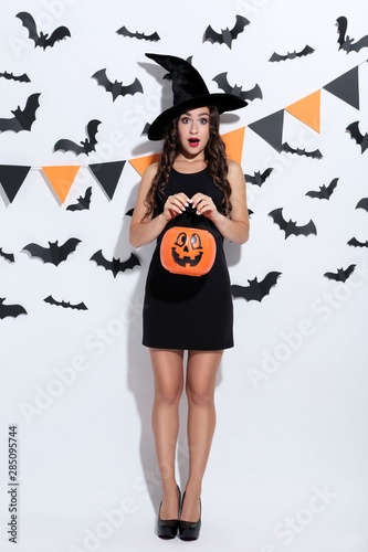 Young woman in halloween costume with pumpkin bucket on white background