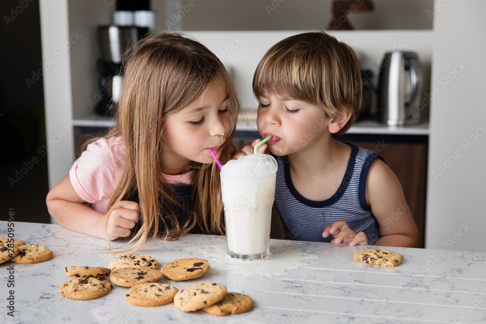 Two kids blowing bubbles in a glass of milk with straws Two kids blowing bubbles in a glass of milk with straws