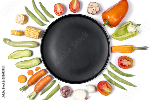 Creative layout made of haricot, tomatoes, pepper, carrot, garlic, corn, zucchini, onion and black plate. Organic food background. Flat lay, top view, copy space. Healthy eating concept.