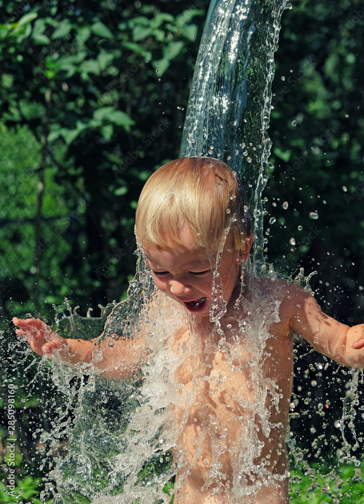 Fototapeta premium Little boy is poured with cold water from bucket. Kids water games on hot day in backyard. Hardening for health. Strengthen your body. Staying cool in summer