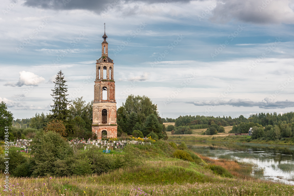 Abandoned bell tower and the Russian cemetery on the background of the rural landscape