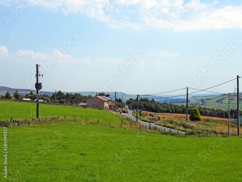 houses in the village of blackshaw head in west yorkshire with a road running thought fields with distant farmhouses and pennine hills against a blue summer sky photo