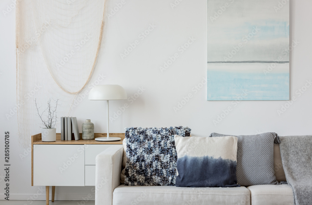 Abstract paste blue and white painting on empty white wall behind beige couch with pillows - obrazy, fototapety, plakaty 