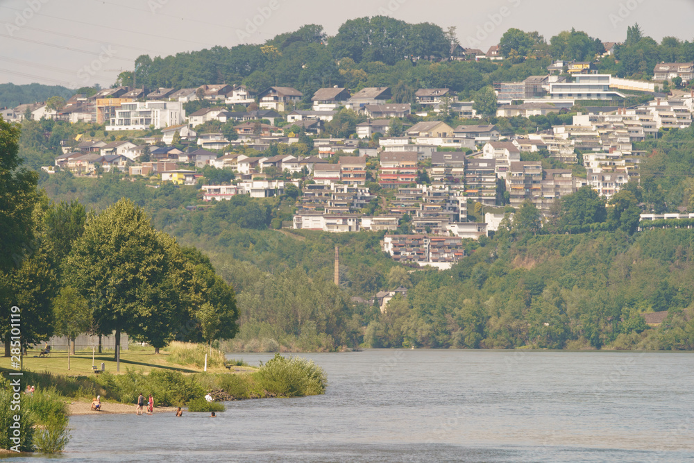 Public beach of river Moselle and swimming citizens. Koblenz cityscape in hot summer day.