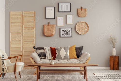 Wooden and wicker accessories in fashionable scandinavian living room interior with futon sofa with pillows