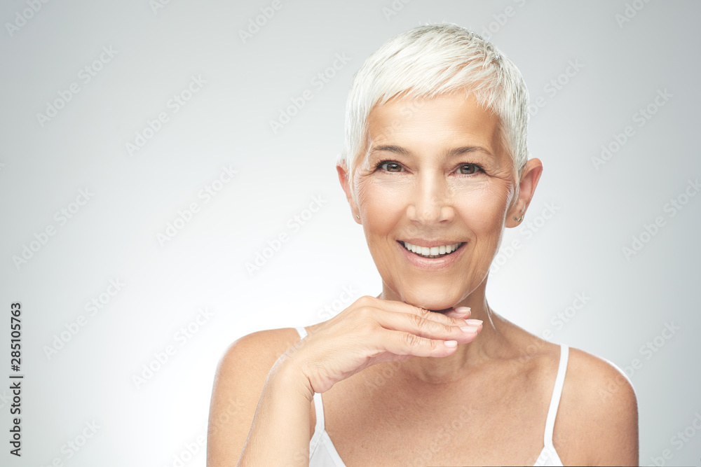 Beautiful smiling senior woman with short gray hair posing in front of gray background. Beauty photography. Beautiful smiling senior woman with short gray hair posing in front of gray background. Beauty photography.