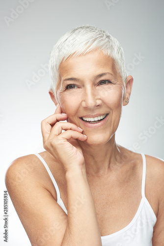 Beautiful smiling senior woman with short gray hair posing in front of gray background. Beauty photography.