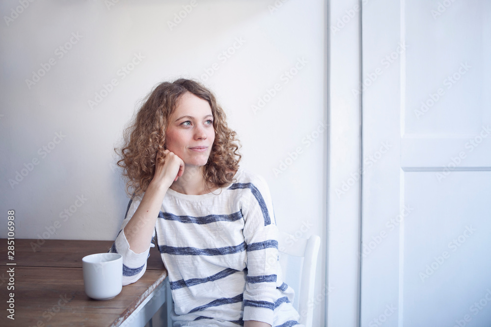 Germany, Bavaria, Munich, Young woman sitting at table, looking away Germany, Bavaria, Munich, Young woman sitting at table, looking away