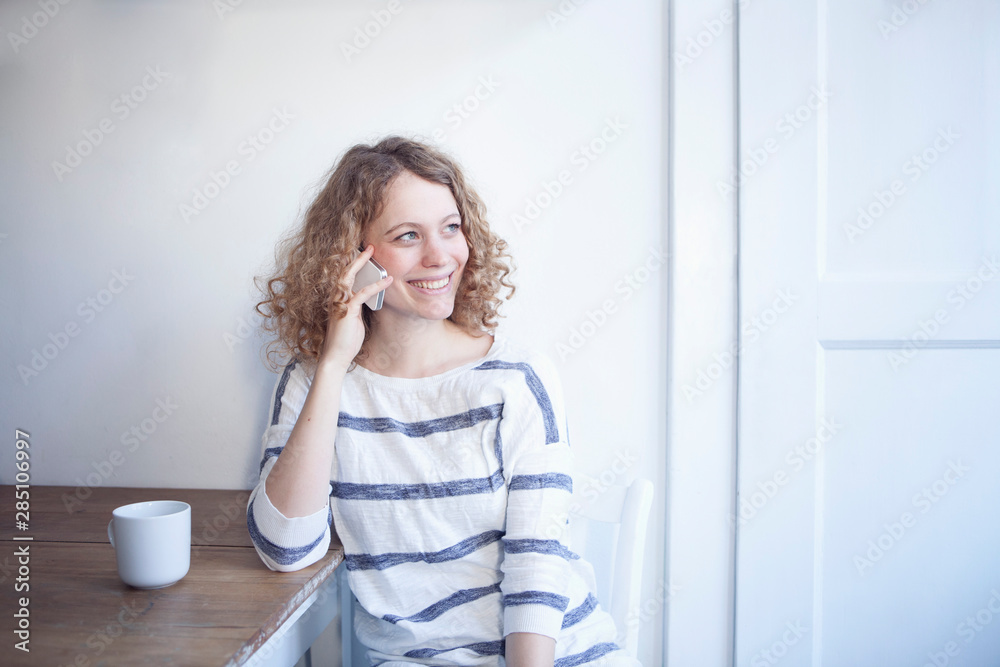 Germany, Bavaria, Munich, Young woman sitting at table and talking on mobile, smiling Germany, Bavaria, Munich, Young woman sitting at table and talking on mobile, smiling