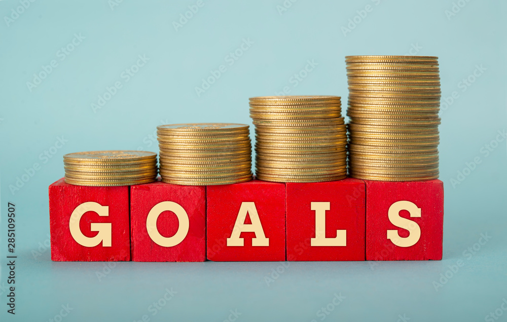 Goals word wrritten on wooden blocks with Coin Stack going up Goals word wrritten on wooden blocks with Coin Stack going up