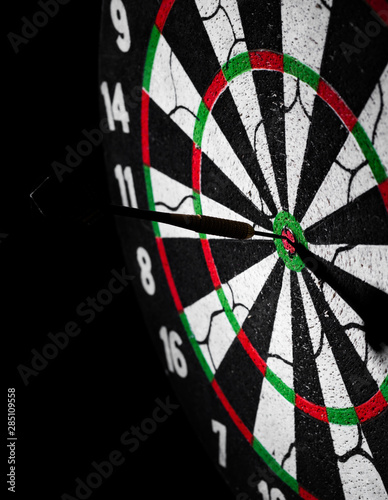 Dartboard with dart arrow hitting the center on a dark black background with copy space.