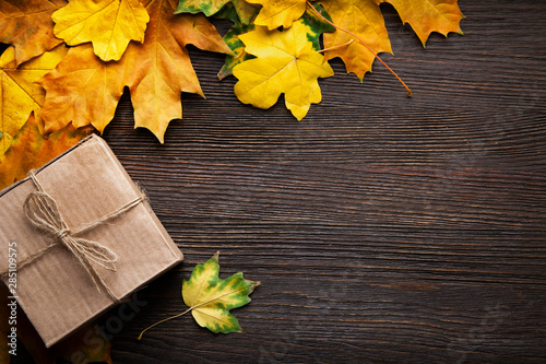 cardboard box tied with string on a bow on a wooden background in autumn leaves, holiday gift on Thanksgiving Hellouin. view from the top. copy space photo