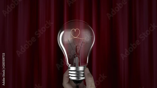 Hand holding lighting bulb with heart words wire shape red curtain background, 3D rendering animation, macro view