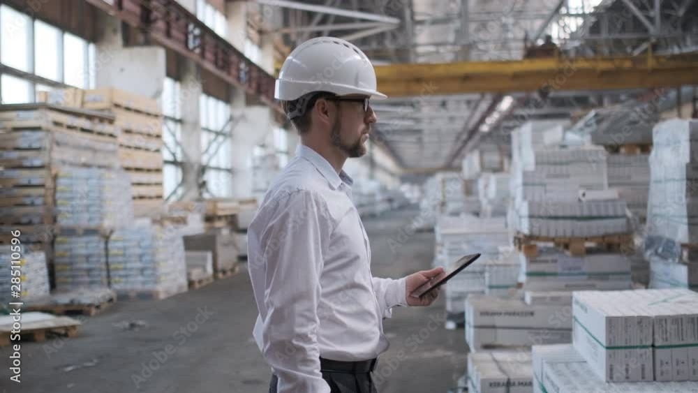 Employee male warehouse worker engineer man in hard hat working at construction site warehouse, walking in logistics center factory, engineer using tablet computer, architect businessman man indoors Employee male warehouse worker engineer man in hard hat working at construction site warehouse, walking in logistics center factory, engineer using tablet computer, architect businessman man indoors