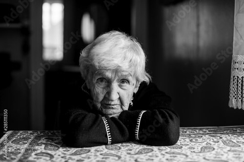 Elderly woman sitting in a dark room, black and white portrait.