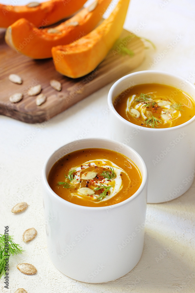 Roasted pumpkin and carrot soup with cream and pumpkin seeds on two white mug on white background with black bread slices.Vegetarian eating.Diet and healthy food concept.Space for copy and text Roasted pumpkin and carrot soup with cream and pumpkin seeds on two white mug on white background with black bread slices.Vegetarian eating.Diet and healthy food concept.Space for copy and text