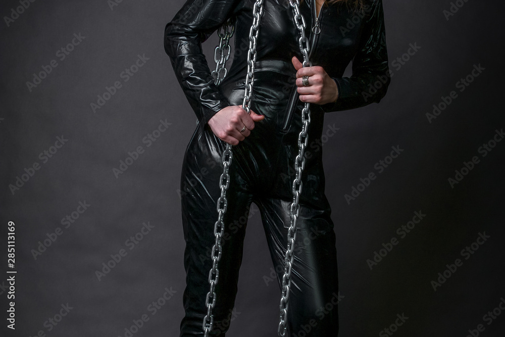 dominant girl in black tight clothes  with chain in hands in Studio on dark background