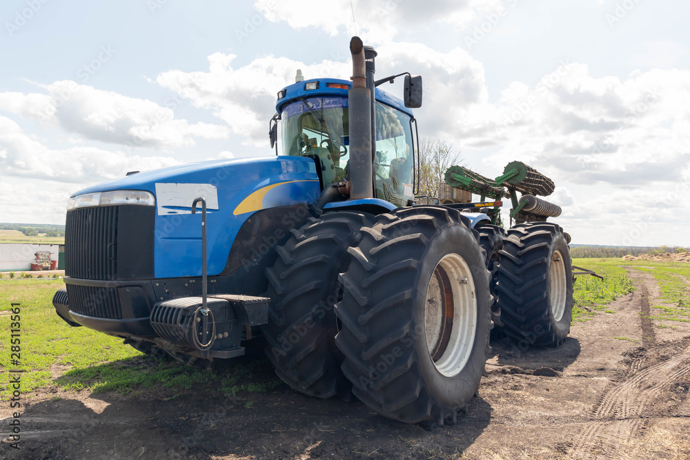 A large, multi-wheeled, blue tractor stands in a field with a green disc plow.A large, multi-wheeled, blue tractor stands in a field with a green disc plow. A large, multi-wheeled, blue tractor stands in a field with a green disc plow.A large, multi-wheeled, blue tractor stands in a field with a green disc plow.