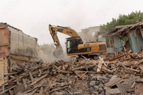 Dismantling (demolition) of an old, dilapidated residential building. Excavator demolishes a house with a bucket.
