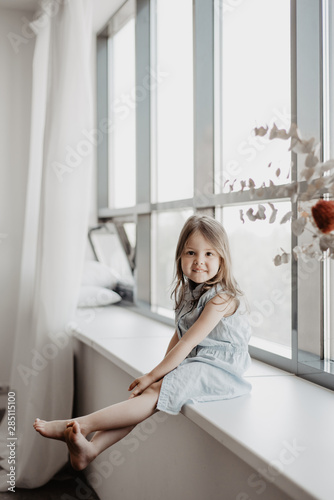 Beautiful little girl sitting on window sill