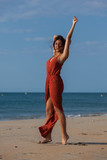 Pretty young woman in a red dress and nude foots on the sand of the beach. Happy girl enjoying freedom at the sea..