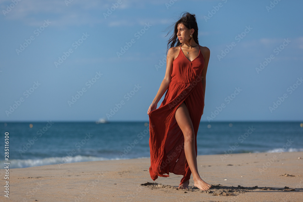 Pretty young woman in a red dress and nude foots on the sand of the beach.  Happy girl enjoying freedom at the sea.. Stock Photo | Adobe Stock