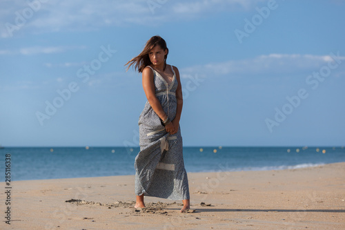Pretty young woman in a dress and nude foots on the sand of the beach. Happy girl enjoying freedom at the sea..