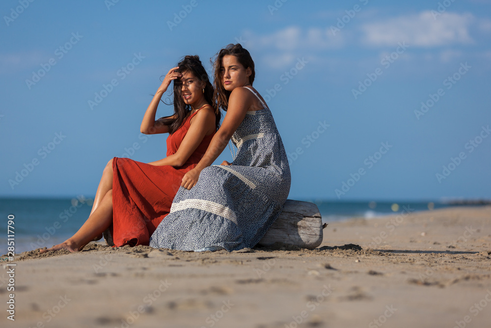 Complicity of two friends girls sitting on driftwood on the beach. Happiness Lifestyle Friendship Concept..