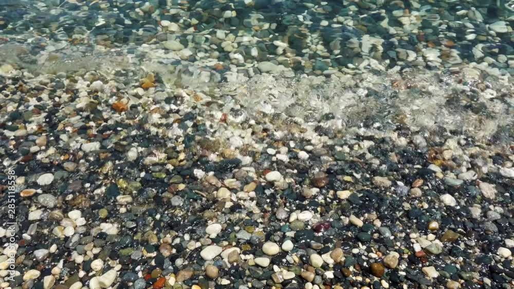 View of blue Mediterranean sea with pebbles. Close up of seawater waves splashing against small rocks at surf View of blue Mediterranean sea with pebbles. Close up of seawater waves splashing against small rocks at surf