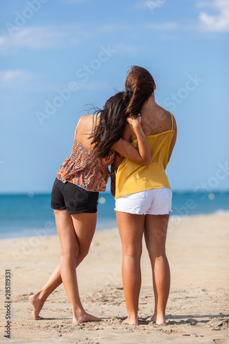 Complicity moment beetwen two girls best friends at the beach. Beautiful young women facing the sea..