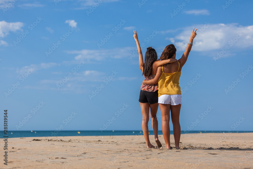 Complicity moment beetwen two girls best friends at the beach. Beautiful young women facing the sea.. Complicity moment beetwen two girls best friends at the beach. Beautiful young women facing the sea..