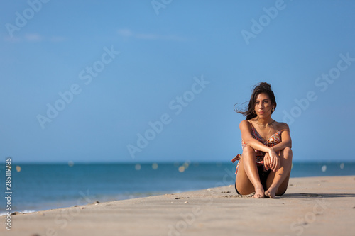 Calm young woman sitting alone on a sand beach. Relaxing and harmony concept..