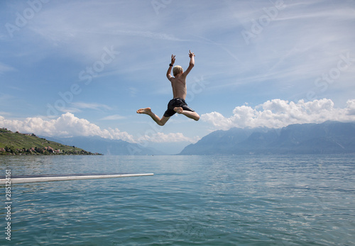 A boy leaping from a diving board over a lake