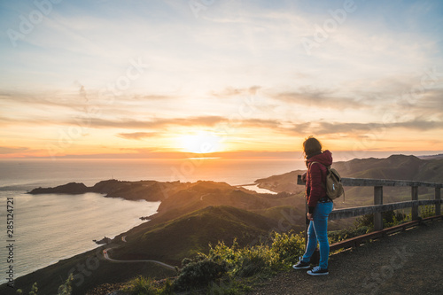 Girl solo traveler watching a beautiful sunset over the Pacific Ocean on top of a hill © icephotography