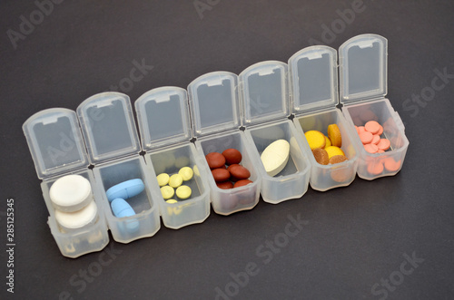 Plastic daily organizer for pills, box with different pills on black background with a copyspace, top view