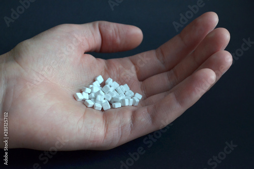 White small square pills lie in the male palm on a black background, side view