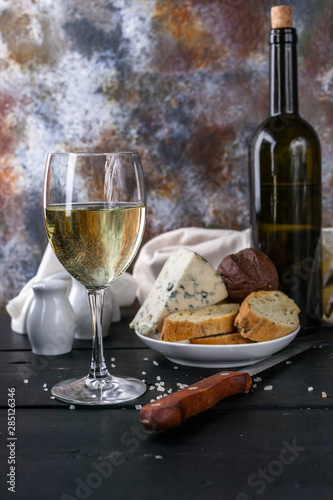 Still life glass of white wine, cheese, bread and a bottle of wine. Low key lighting. Vertical shot