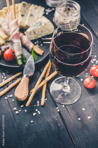 Close-up glass of red wine, snacks, jamon, cheese, cherry tomatoes and arugula. Vertical shot © yusev