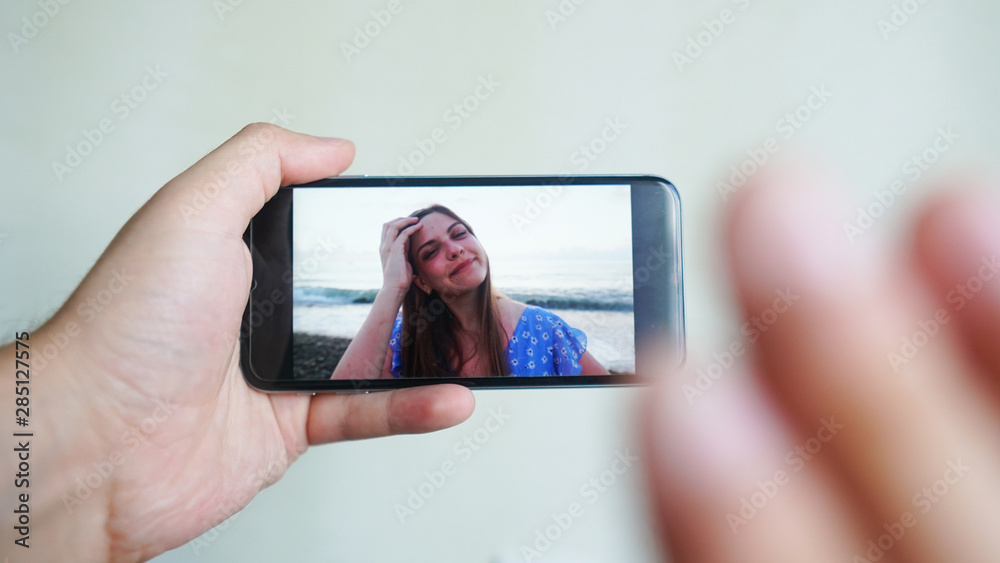 Beautiful girl smiling at boyfriend from mobile phone screen. Couple chatting via video call application. Long distance relationship, virtual communication. Close up view 