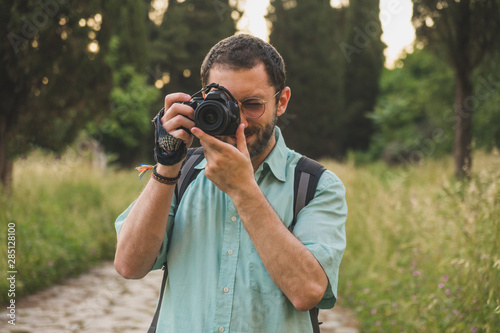 Young photographer focusing and taking a picture towards the camera in the park