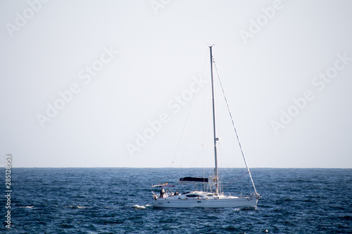 A sailing boat in a mediterranean blue sea, horizon landscape with a white sky with seagulls flying over.