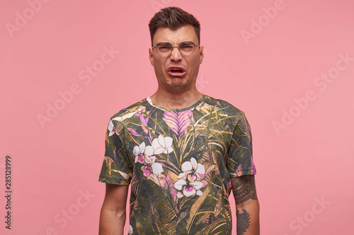 Wallpaper Mural Portrait of young short-haired man looking at camera, showing disgust, wearing t-shirt with floral print and glasses, standing over pink background Torontodigital.ca