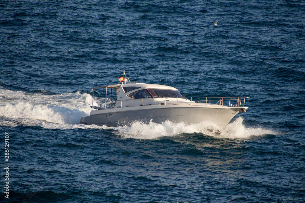 Fototapeta premium Small white yacht in Spanish sea with blue water creating waves.