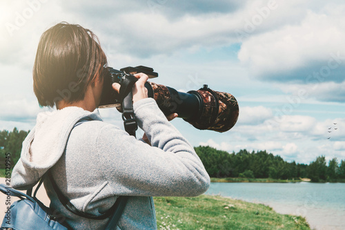 Young woman with a camera with a telephoto lens, photographing birds on the lake. Wildlife photographer at work. Minsk, Belarus.