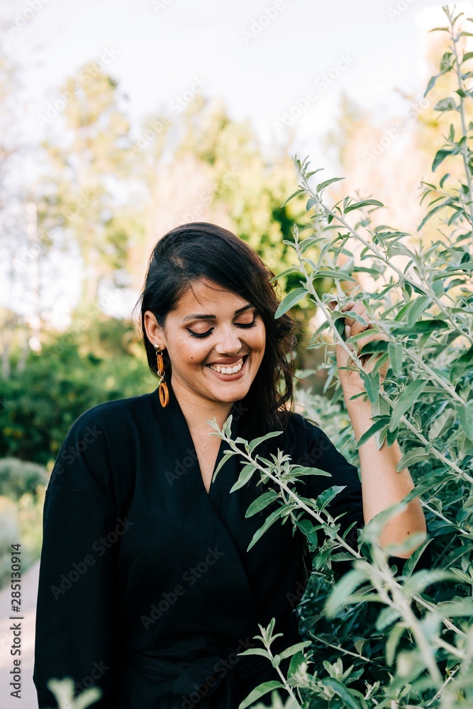 Beautiful brunette woman standing among blooming bushes in park and looking away in Lisbon