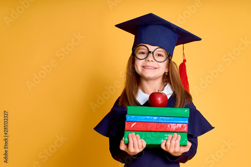 School Girl in academician clothes with book and apple on yellow stduio background photo