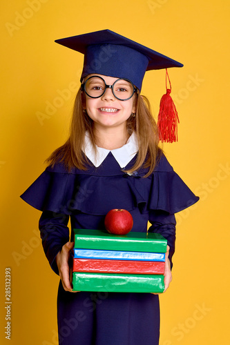 School Girl in academician clothes with book and apple on yellow stduio background photo