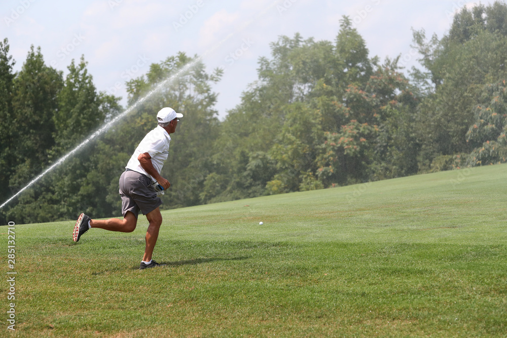 Golfers play as sprinkler systems water the golf course.